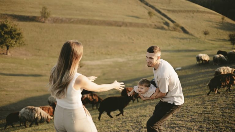 A joyful family with a child in a pastoral setting, embracing countryside life with grazing sheep.